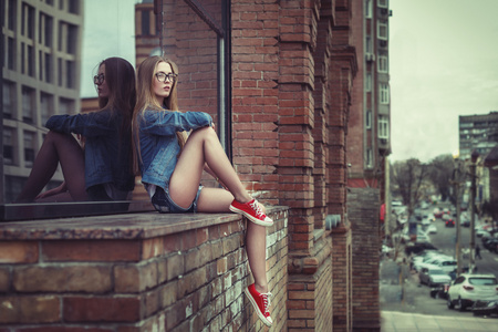 户外生活方式的年轻漂亮坐在女孩，穿着时髦赃物 grunge 风格城市背景的肖像。复古复古健美的形象，电影仿真
