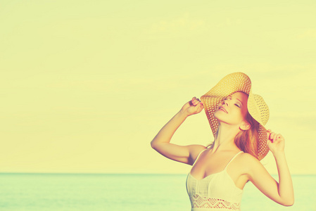 美丽幸福的女人，戴着帽子在日落海滩上享受过海