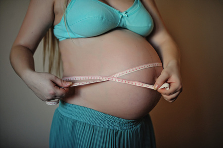 孕妇拿着米磁带在她的婴孩碰撞