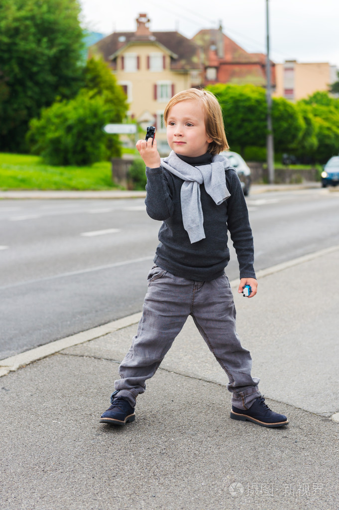 室外肖像的可爱时尚男孩在街头,穿着灰色的衣服和暗蓝色的鞋子