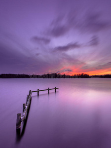 宁静的湖面上紫色的夕阳和木制的系泊柱