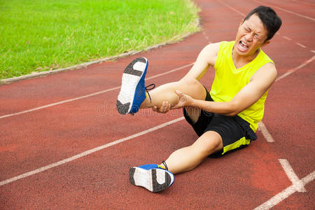 在跑道上腿抽筋的年轻男运动员照片