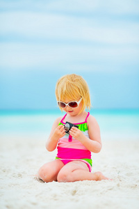 坐在海滩上的照片相机太阳镜女婴