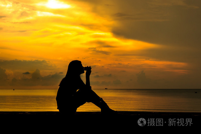 轮廓的日落海滩附近喝咖啡的女人