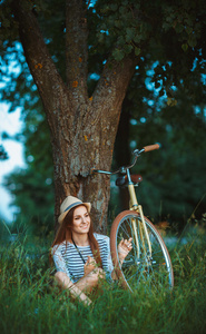 可爱的年轻女子在一辆自行车在户外一顶帽子