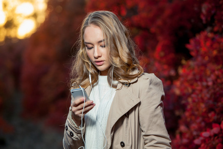 年轻貌美的女人写作消息上的手机在一个秋天的公园