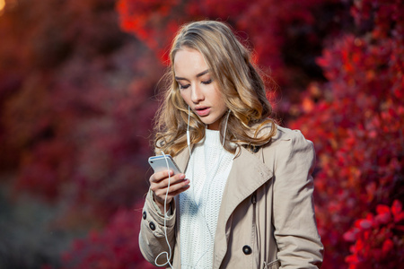 年轻貌美的女人写作消息上的手机在一个秋天的公园