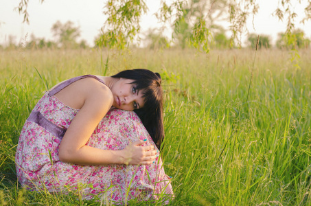 美丽伤心的女孩，独自坐在草地上在阳光灿烂的夏天的一天