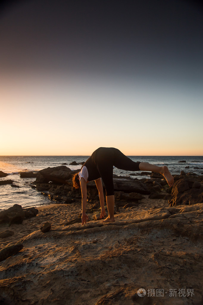 剪影年轻女子在日落时练瑜伽在海滩上
