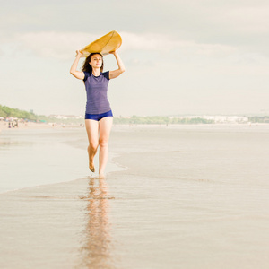 美丽冲浪女孩在大洋彼岸，夕阳漫步海滩上的黄色冲浪板在她的手。健康的生活，体育概念与 copyspace