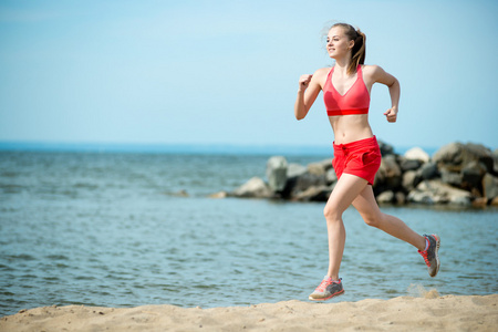 年轻的女士在阳光灿烂的夏天砂沙滩上运行。锻炼。慢跑