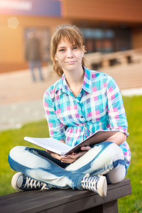 女学生与本抄写本在长凳上。夏校园公园
