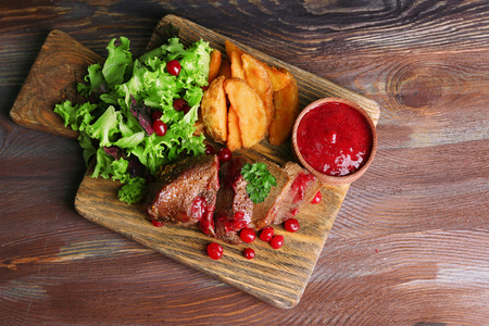 牛肉调味蔓越莓酱，烤的土豆切片在砧板上木制的背景上