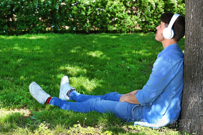 男人戴着耳机在公园树下休息