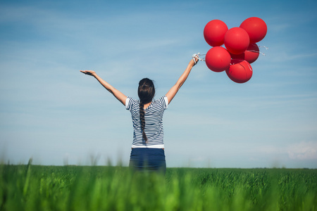 在一片绿色的草地上一个红气球的幸福年轻女人