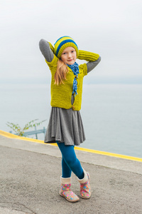 可爱的小女孩在寒冷的日子，在户外玩舞美丽的湖，穿着绿色的毛衣 帽子和温暖的靴子