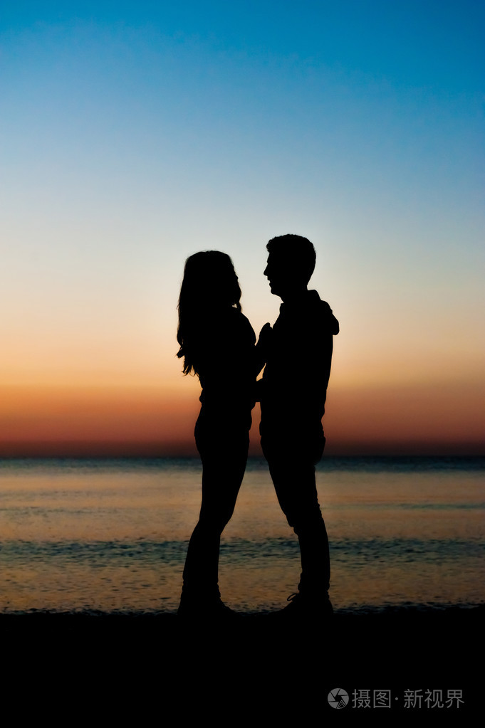 夫妻彼此在沙滩上面临日出的剪影