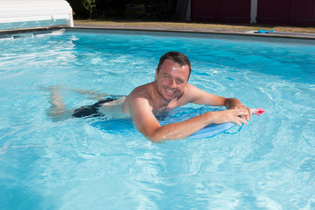 男子游泳与他的冲浪板，在蓝色的水游泳和微笑