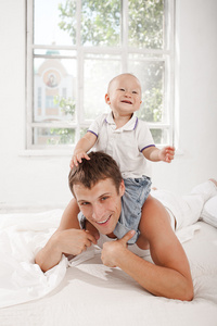 年轻的父亲与他九个月大的儿子在家里的床上