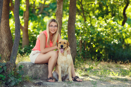 美丽的年轻女孩的肖像与她的狗拉布拉多猎犬户外在夏季美丽的公园