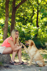 美丽的年轻女孩的肖像与她的狗拉布拉多猎犬户外在夏季美丽的公园