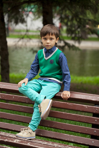 小男孩坐在一个夏天公园的长椅上
