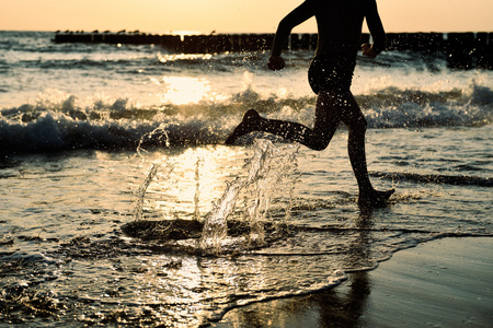 在海边男孩在日落时分在沙滩上跑