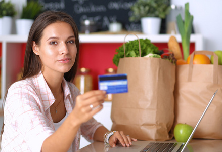 面带笑容的女人，网上购物在厨房中使用平板电脑和信用卡