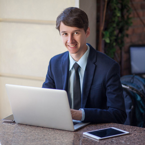 一个轻松年轻英俊专业商人使用自己的笔记本电脑 手机和平板电脑在一个喧闹的咖啡馆