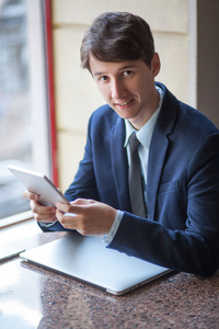 一个轻松年轻英俊专业商人使用自己的笔记本电脑 手机和平板电脑在一个喧闹的咖啡馆