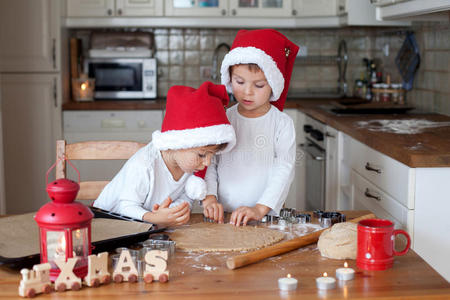 两个戴圣诞帽的可爱男孩在厨房里准备饼干