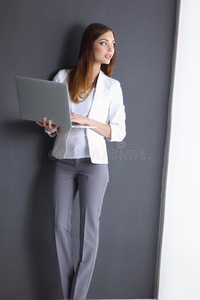 一个拿着笔记本电脑的年轻女人，穿着灰色的衣服