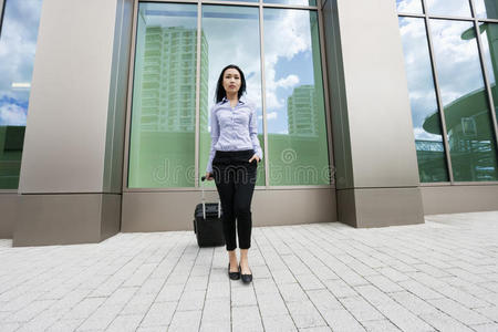 亚洲年轻的女商人，带着手提箱在人行道上反对建筑