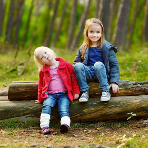 两个小妹妹坐在森林里的一根木头上