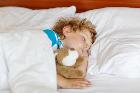 一个金发的小孩和玩具睡在床上。