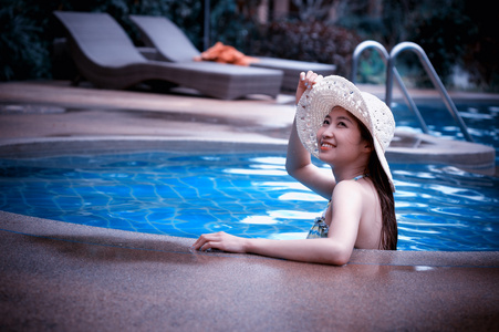 亚洲美丽的女人，在游泳池放松的大帽子