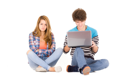在恋爱中的一对漂亮的年轻夫妇的肖像, 在白色背景上被孤立坐在地板上, 他在她疯了的时候看电脑