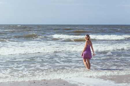 年轻漂亮苗条的女孩站在沙滩上阳光明媚的夏日，海上大风