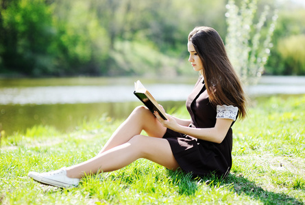 女生拿着一本书放松在公园的草地上