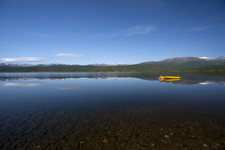 在宁静的湖与雪覆盖的山上的黄色小船, 挪威