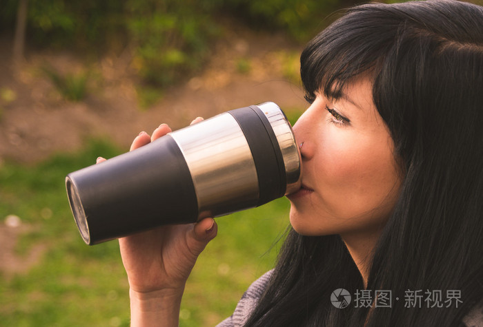 黑发的西班牙裔女人户外花园环境从银黑色咖啡杯子喝水