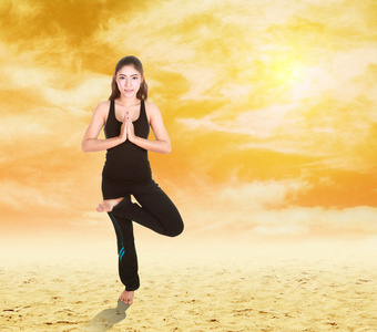 女人在日落时分在天空沙上瑜伽锻炼