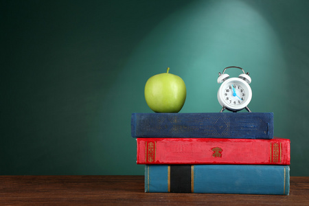 一摞书与闹钟和青苹果绿色黑板背景