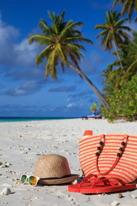 秸秆育肥的帽子，袋子，太阳眼镜和拖鞋在沙滩上