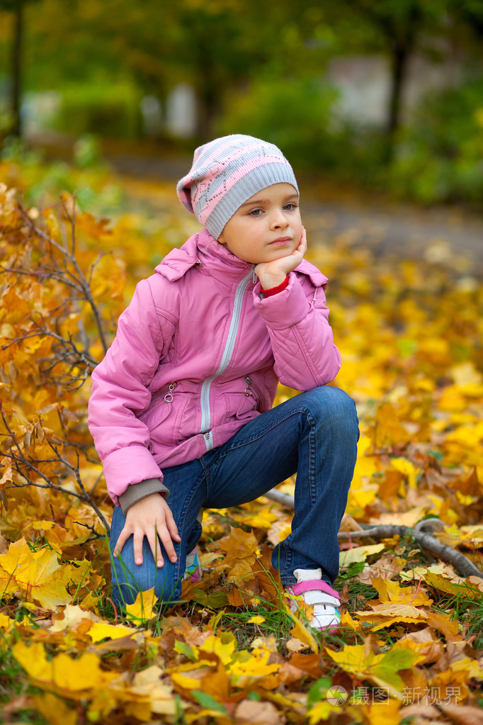 漂亮的小女孩,在一个粉红色的外套和帽子上秋天背景