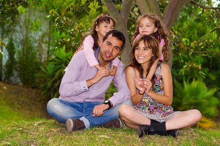 家庭肖像的父亲 母亲和两个女儿一起坐在花园的环境中，儿童背后父母拥抱着他们笑得好开心