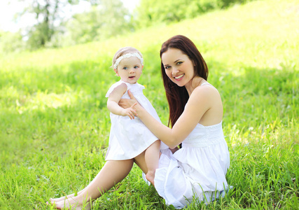 快乐微笑妈妈和宝宝坐在阳光明媚的汇总在草地上