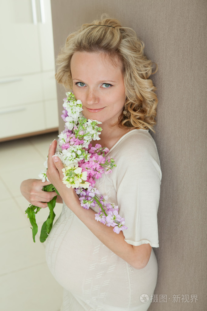 美丽的怀孕女性在家里看着摄像机