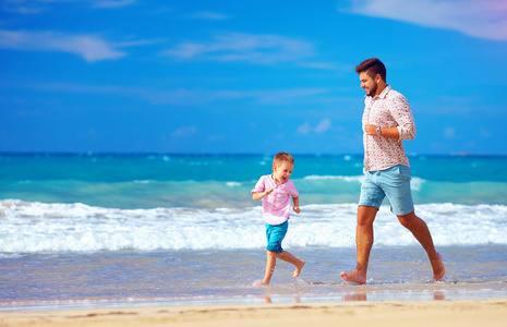 快乐兴奋的父亲和儿子运行在夏天的海滩，享受生活