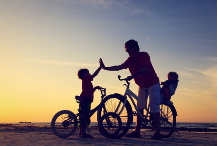 骑自行车在日落时的两个孩子的父亲
